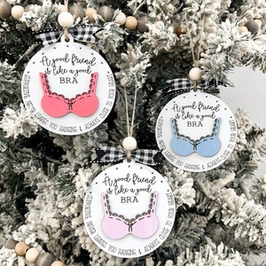May include: Three white round ornaments with black and white checkered ribbon. Each ornament has a pink or blue bra cutout with the text "A good friend is like a good BRA" and "SUPPORTIVE NEVER LEAVES YOU HANGING & ALWAYS CLOSE TO YOUR HEART".