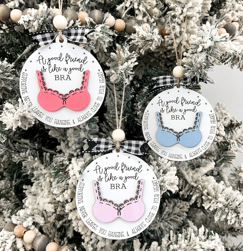 May include: Three white round ornaments with black and white checkered ribbon. Each ornament has a pink or blue bra cutout with the text "A good friend is like a good BRA" and "SUPPORTIVE NEVER LEAVES YOU HANGING & ALWAYS CLOSE TO YOUR HEART".
