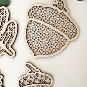 May include: Two wooden acorn-shaped ornaments with a woven pattern. The ornaments are made of light brown wood and have a delicate, intricate design.