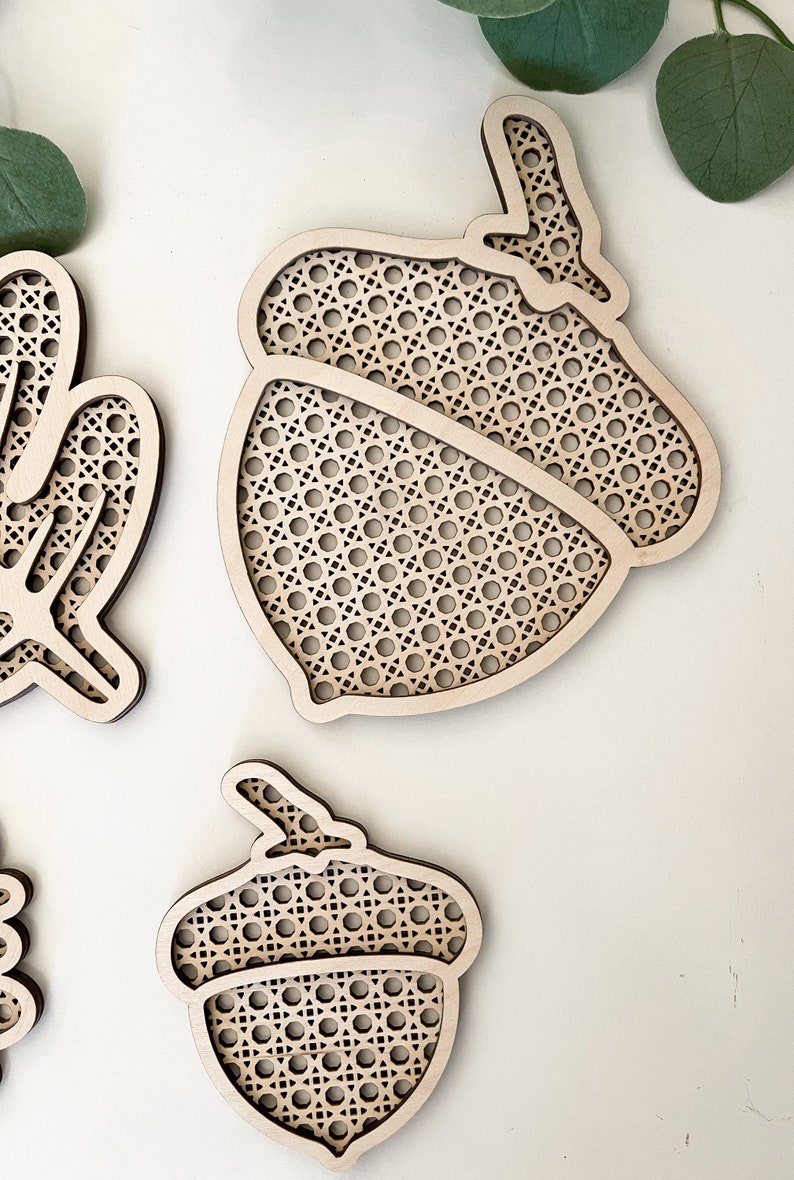 May include: Two wooden acorn-shaped ornaments with a woven pattern. The ornaments are made of light brown wood and have a delicate, intricate design.
