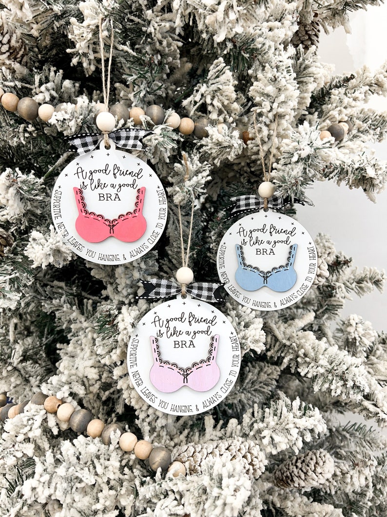 May include: Three white round ornaments with black and white checkered ribbon. Each ornament has a pink, blue, or white bra cutout with the text "A good friend is like a good BRA" and "SUPPORTIVE NEVER LEAVES YOU HANGING & ALWAYS CLOSE TO YOUR HEART".