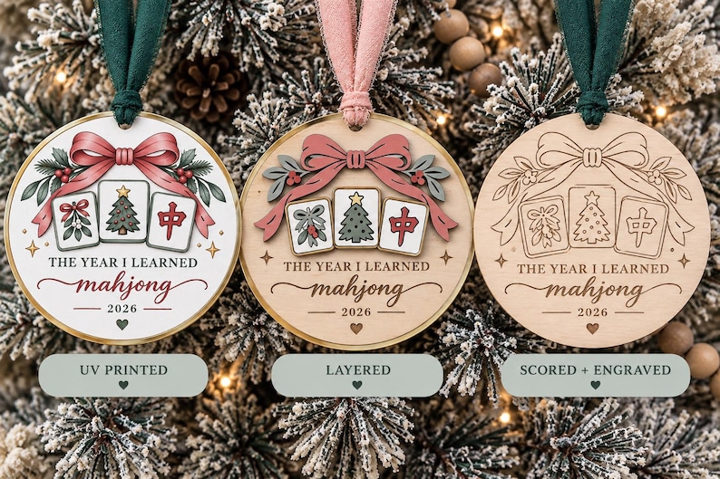 May include: Three round wooden ornaments with green or pink ribbons. Each features a bow, holly, and three mahjong tiles with a Christmas tree and the text THE YEAR I LEARNED mahjong 2026. Styles include UV printed, layered, and scored and engraved.