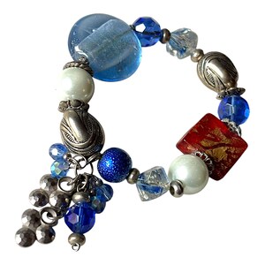 May include: A beaded bracelet featuring a mix of blue, silver, and red beads. The bracelet includes large blue glass beads, silver-toned metal accents, and a cluster of dangling silver beads. A red square bead with gold accents adds a pop of color.