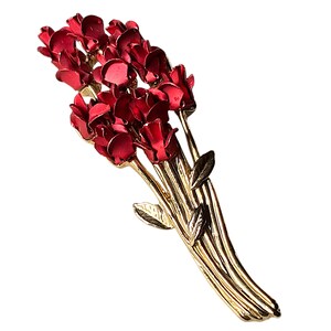 Può includere: Una spilla in metallo color oro a forma di bouquet di rose smaltate di rosso. Il pezzo presenta diversi boccioli di colore rosso intenso raggruppati in alto, con lunghi steli dorati sottili e piccole foglie dorate che scendono verso la base.