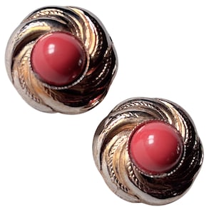Peut inclure: Une paire de boucles d'oreilles vintage. Chaque boucle d'oreille présente un motif tourbillonnant argenté entourant un centre rond de couleur corail. Les boucles d'oreilles sont sur fond blanc, mettant en valeur les détails et le contraste des couleurs.