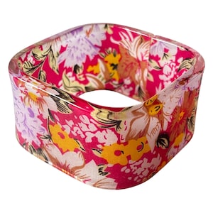 Peut inclure: Un bracelet jonc carré avec un motif floral. Le bracelet présente un extérieur transparent et clair avec un motif intérieur vibrant de fleurs roses, jaunes, blanches et violettes. Un accessoire de mode audacieux.