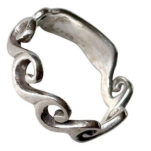 Könnte beinhalten: Ein silberfarbener Metallring mit einem durchgehenden Banddesign, das mehrere erhabene, geschwungene Spiralmuster aufweist, die sich um den Umfang des Stücks winden. Das Metall hat eine polierte Oberfläche mit sichtbarer Tiefe in den vertieften Bereichen.