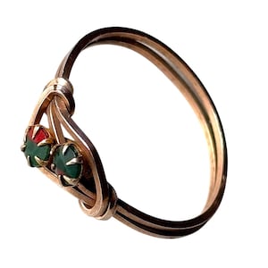 May include: A gold-coloured bracelet featuring two gemstones. One gemstone is red, the other is green. The bracelet has a distinctive knot design, and the gemstones are set in gold-coloured metal.