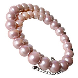 May include: A double-strand bracelet composed of round, light pink pearls of varying sizes. The bracelet features a silver-toned metal chain extension with a small spherical bead at the end, allowing for adjustable sizing on the wrist.
