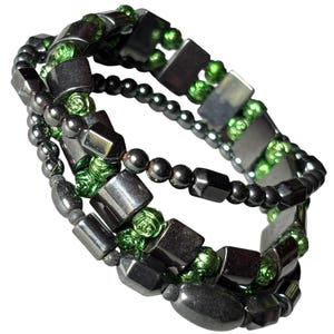 May include: A multi-strand bracelet featuring alternating dark gray metallic rectangular beads and small, round, vibrant green beads. The design incorporates a mix of smooth, polished dark gray cylindrical and rectangular components throughout.