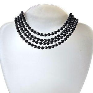 May include: A five-strand black beaded necklace displayed on a white mannequin bust. The necklace features small, round, glossy black beads. The beads are evenly spaced, creating a layered effect. The background is plain white.