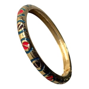 Pode incluir: Pulseira de bracelete dourada com um padrão decorativo. O padrão apresenta detalhes em esmalte vermelho, azul e castanho escuro. A pulseira tem formato circular e parece ser feita de metal.