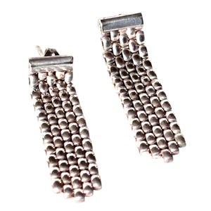 Peut inclure: Une paire de boucles d'oreilles pendantes argentées. Chaque boucle d'oreille présente un dessus rectangulaire et une série de petites perles arrondies en cascade, créant un effet de frange. Sur fond blanc.