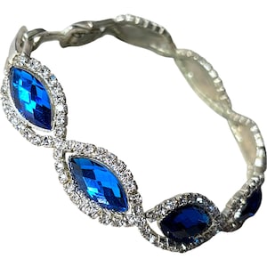 May include: Silver-toned bracelet featuring alternating marquise-shaped blue gemstones and clear crystals. The bracelet has a twisted, openwork design. The blue gemstones are a deep, vibrant color, and the crystals sparkle.