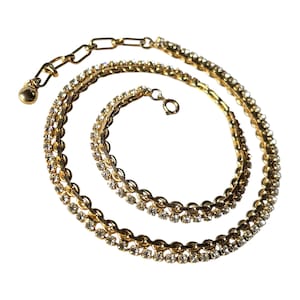 Puede incluir: Un collar dorado con un diseño de doble cadena. El collar presenta pequeños y brillantes pedrería a lo largo de la cadena. El cierre y la cadena ajustable también son dorados. Esta elegante pieza es adecuada para ocasiones especiales.