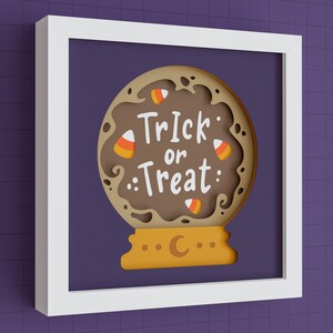 May include: A white frame with a brown paper mache Halloween-themed papercraft inside. The papercraft is a brown and orange globe with the words "Trick or Treat" and candy corn decorations.