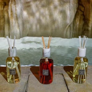 Puede incluir: Tres difusores de varillas de cristal con tapones de mármol blanco y varillas de madera. Dos botellas contienen líquido amarillo claro y la botella central contiene líquido rojo. Cada etiqueta lleva el texto Profumi del Marmo.