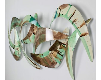 May include: Abstract wall art sculpture made of metal with a green, brown, and white paint finish. The sculpture is made of multiple curved pieces of metal that are joined together.