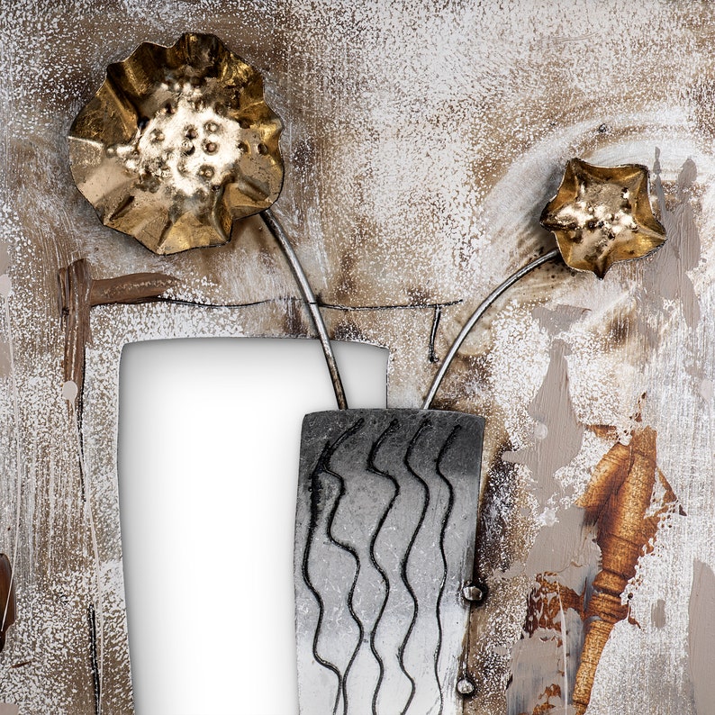 May include: A metal wall art piece featuring a vase with two stylized flowers. The vase is silver with a wavy pattern and the flowers are gold with a textured surface. The background is a light brown with white and gray accents.