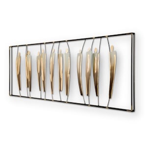 Op de afbeelding: Een metalen wandsculptuur met een reeks abstracte figuren in goud- en grijze tinten. De figuren zijn in een rij gerangschikt binnen een zwart metalen frame.