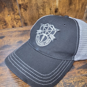 Op de afbeelding: Een zwarte en grijze baseballpet met een mesh achterkant. De pet heeft een grijs geborduurd patch met de woorden "De Oppresso Liber" en een ontwerp met gekruiste zwaarden.