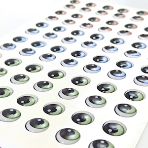 K&ouml;nnte beinhalten: Eine Blatt mit bunten Plastik-Glitz Augen, perfekt f&uuml;r Bastelprojekte. Die Augen sind in verschiedenen Gr&ouml;&szlig;en und Farben erh&auml;ltlich, darunter Blau, Gr&uuml;n und Braun.