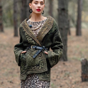 May include: A woman wearing a green quilted jacket with a leopard print skirt and a gold necklace. She is standing in a forest.