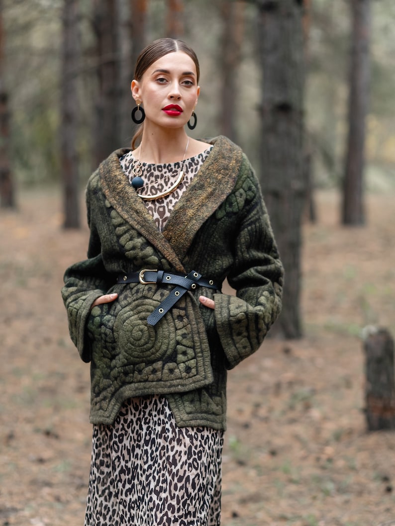 May include: A woman wearing a green quilted jacket with a leopard print skirt and a gold necklace. She is standing in a forest.