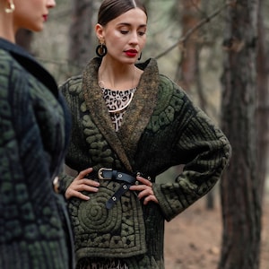 May include: Two women wearing green jackets with intricate patterns. One woman is wearing a leopard print skirt and a gold necklace. Both women are wearing large black earrings.
