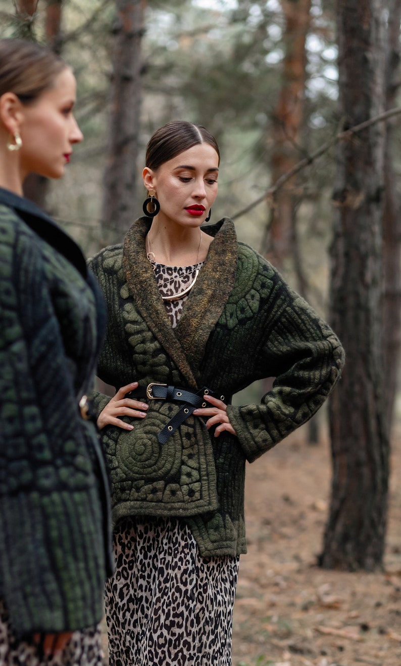 May include: Two women wearing green jackets with intricate patterns. One woman is wearing a leopard print skirt and a gold necklace. Both women are wearing large black earrings.