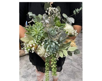 May include: A bridal bouquet featuring a variety of succulents, white flowers, and greenery. The bouquet has a cascading design with long trailing stems.