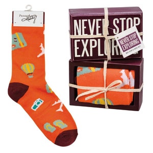 May include: Orange socks with a travel theme print, packaged in a box with the words "Never Stop Exploring".