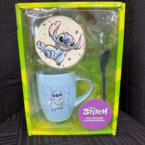 Puede incluir: Un juego de taza, posavasos y cuchara de Disney Stitch. La taza azul claro tiene el texto "WEIRD BUT CUTE" y un gr&aacute;fico de Stitch. El posavasos presenta a Stitch. El juego est&aacute; empaquetado en una caja verde y amarilla.