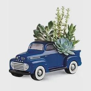 May include: A blue ceramic truck planter with white-walled tires, filled with various green succulents. The truck features a classic design with a detailed front grille and a vintage aesthetic. The plants add a natural element to the decorative piece.