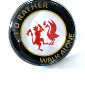 Puede incluir: Un botón redondo, blanco y negro con el texto "I'D RATHER WALK ALONE" en letras doradas. El centro presenta un diablo rojo y un pájaro rojo. El botón es probablemente un pin o una insignia.