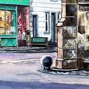 May include: Watercolour painting of a European street scene. Buildings with white and brown facades, a green awning, and a bench. The street is light purple, with a bollard in the foreground. A quaint, artistic depiction.