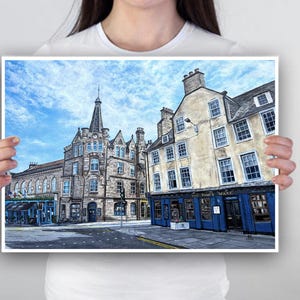 May include: A print depicting a street scene with stone buildings under a cloudy blue sky. One building features a sign reading "The Times Wark". The architecture includes multiple windows and a prominent spire.