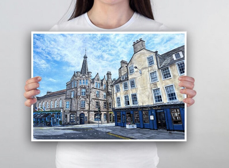 May include: A print depicting a street scene with stone buildings under a cloudy blue sky. One building features a sign reading "The Times Wark". The architecture includes multiple windows and a prominent spire.