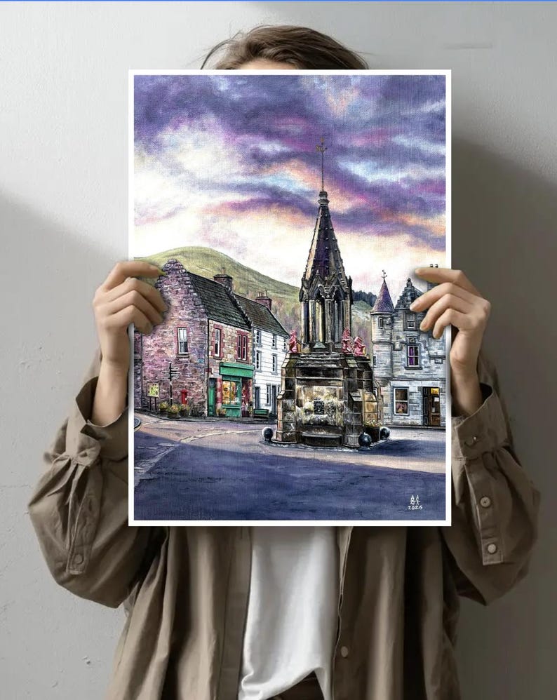May include: Watercolour print depicting a town square with a stone monument and buildings. The sky is a blend of purple and orange. The artwork is held in front of a person.
