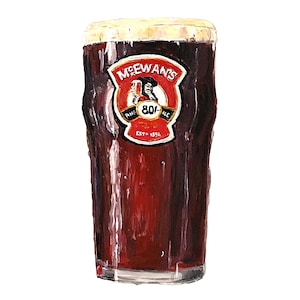 May include: A glass of dark brown beer with a white head. The glass has a label that says "McEwans's" with a pirate logo and the text "Fine 80/- Ale Est. 1856".