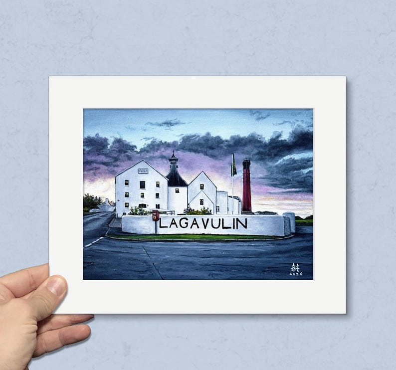 May include: A framed print of the Lagavulin distillery, featuring white buildings, a red smokestack, and the distillery's name. The artwork is set against a dramatic sky with dark clouds and a hint of sunset colors.