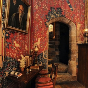 May include: A red and gold tapestry with a unicorn design hangs on the wall of a room with a wooden desk, chair, and a doorway leading to a staircase.