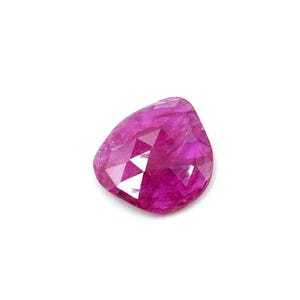 Könnte beinhalten: Ein facettierter, tropfenförmiger Edelstein in leuchtendem Magenta. Die Oberfläche des Edelsteins reflektiert das Licht und zeigt seine komplizierten Schnitte und seine innere Struktur. Der Edelstein ist vor einem weißen Hintergrund platziert.