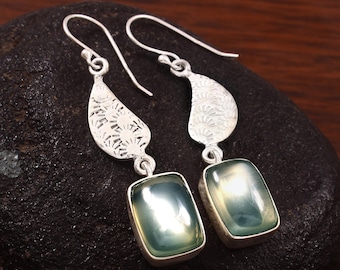 May include: Silver dangle earrings with a green gemstone and a floral design on the top of the earring.