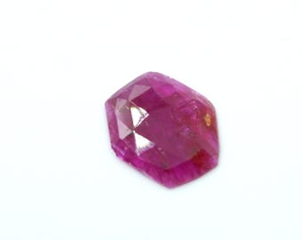Könnte beinhalten: Ein facettierter, sechseckiger Rubin-Edelstein. Der Edelstein hat eine tiefe, gesättigte rosa-rote Farbe mit mehreren Facetten, die das Licht reflektieren. Der Edelstein ist vor einem weißen Hintergrund platziert.
