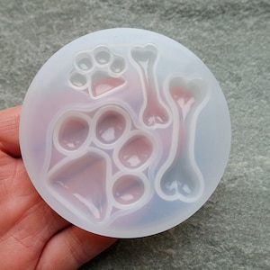 May include: A clear silicone mold with five different shapes: a paw print, a bone, a triangle, and two circles. The mold is designed for making resin crafts.