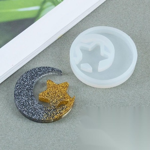 Puede incluir: Un molde de silicona para hacer manualidades de resina. El molde tiene forma de media luna con una estrella en su interior. El molde es blanco y la estrella es transparente.