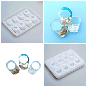 Könnte beinhalten: Eine Silikonform mit acht ringförmigen Vertiefungen zum Herstellen von Harzringen. Die Form ist weiß und hat eine glatte Oberfläche. Es gibt drei fertige Harzringe mit goldenem und blauem Glitzer und ein paar kleinen, bunten Perlen im Inneren.