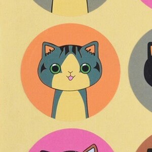 May include: A round sticker with an orange background features a cartoon cat with green eyes, a pink tongue, and gray and yellow fur.