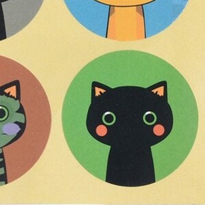May include: A black cat with green eyes and pink cheeks is on a green circle. The cat is looking straight ahead.